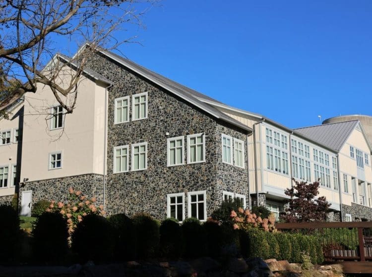 A large modern commercial building featuring a stone facade and a clean white siding. The building's exterior showcases a blend of contemporary and rustic architectural elements with a backdrop of clear blue skies.