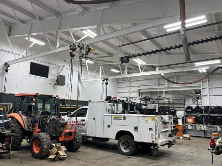 Large workshop featuring an orange tractor and a white service truck under a bright, clean-painted ceiling.